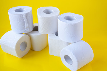 A pile of rolls of white toilet paper on a yellow background