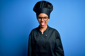 Young african american chef woman wearing cooker uniform and hat over blue background sticking tongue out happy with funny expression. Emotion concept.
