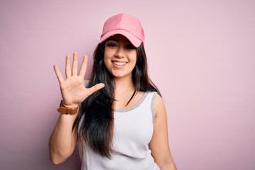 Young brunette woman wearing casual sport cap over pink background showing and pointing up with fingers number five while smiling confident and happy.