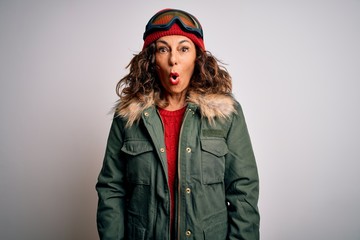 Middle age skier woman wearing snow sportswear and ski goggles over white background afraid and shocked with surprise expression, fear and excited face.
