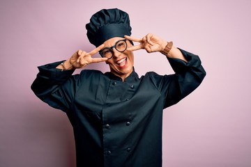 Middle age brunette chef woman wearing cooker uniform and hat over isolated pink background Doing peace symbol with fingers over face, smiling cheerful showing victory