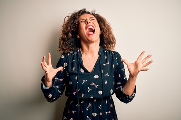 Middle age beautiful woman wearing casual dress standing over isolated white background crazy and mad shouting and yelling with aggressive expression and arms raised. Frustration concept.