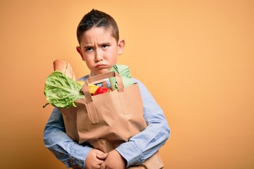 Adorable toddler holding paper bag with food standing over isolated yellow background