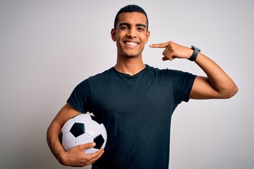 Handsome african american man playing footbal holding soccer ball over white background smiling cheerful showing and pointing with fingers teeth and mouth. Dental health concept.