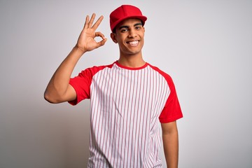Young handsome african american sportsman wearing striped baseball t-shirt and cap smiling positive doing ok sign with hand and fingers. Successful expression.
