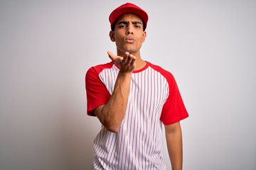 Young handsome african american sportsman wearing striped baseball t-shirt and cap looking at the camera blowing a kiss with hand on air being lovely and sexy. Love expression.