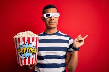 Young handsome african american man watching movie using 3d glasses eating popcorns Pointing aside worried and nervous with forefinger, concerned and surprised expression