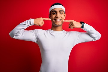 Fototapeta premium Young handsome african american sportsman wearing sportswear over red background smiling cheerful showing and pointing with fingers teeth and mouth. Dental health concept.