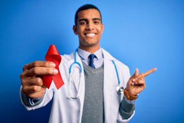 Young handsome african american doctor man holding red HIV ribbon symbol very happy pointing with hand and finger to the side