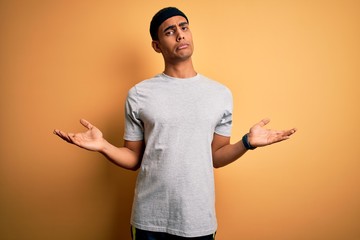 Handsome african american sportsman doing sport wearing sportswear over yellow background clueless...