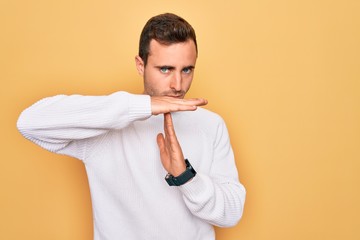 Young handsome man with blue eyes wearing casual sweater standing over yellow background Doing time...
