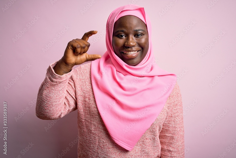 Sticker young african american plus size woman wearing muslim hijab over isolated pink background smiling an