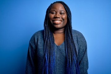 African american plus size woman with braids wearing casual sweater over blue background with a...
