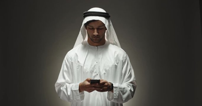 Arabian businessman in traditional white dress talking on phone and positively smiling isolated on black background close up shot 4k