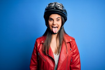 Young beautiful brunette motorcycliste woman wearing motorcycle helmet and jacket sticking tongue out happy with funny expression. Emotion concept.