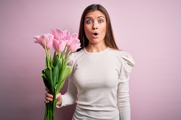 Young beautiful romantic woman with blue eyes holding beauty bouquet of pink tulips scared in shock with a surprise face, afraid and excited with fear expression