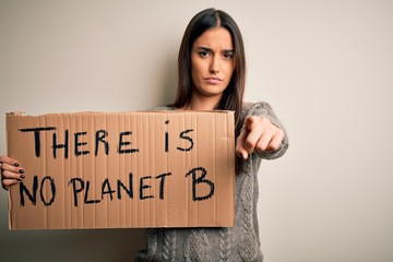 Young beautiful brunette activist woman protesting for save the planet holding banner pointing with finger to the camera and to you, hand sign, positive and confident gesture from the front
