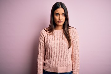 Young beautiful brunette woman wearing casual sweater over isolated pink background skeptic and...