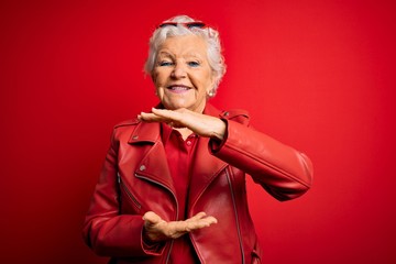Senior beautiful grey-haired woman wearing casual red jacket and sunglasses gesturing with hands showing big and large size sign, measure symbol. Smiling looking at the camera. Measuring concept.