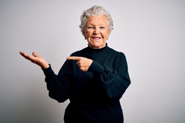 Senior beautiful woman wearing casual black sweater standing over isolated white background amazed and smiling to the camera while presenting with hand and pointing with finger.