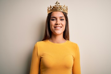 Young beautiful brunette woman wearing golden queen crown over white background with a happy and cool smile on face. Lucky person.