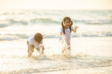 Happy little Asian brother and sister running and playing with smiling and laughing together on the beach at sunset. Adorable kids girl and boy relax and having fun in summer holiday vacation travel. - Powered by Adobe