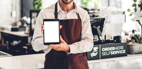 Portrait of barista man small business owner standing with tablet computer with white mockup blank in the cafe or coffee shop in a cafe