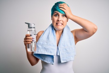 Young sporty woman with blue fashion hair holding bottle of water wearing towel after do sport stressed with hand on head, shocked with shame and surprise face, angry and frustrated. Fear and upset 