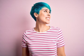 Young beautiful woman with blue fashion hair wearing casual striped t-shirt looking away to side with smile on face, natural expression. Laughing confident.