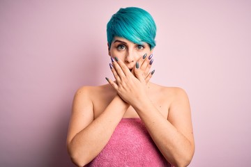 Young woman with blue fashion hair wearing towel after shower over pink background shocked covering mouth with hands for mistake. Secret concept.