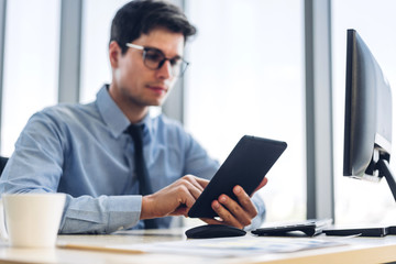 Handsome confident businessman relaxing looking at technology of tablet computer while sitting on chair.Young creative coworkers manager business people during working day with cup of coffee at office