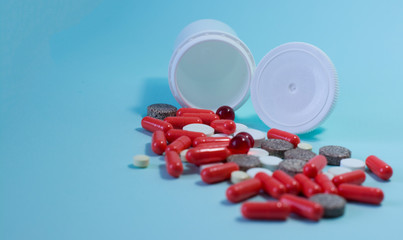 a handful of pills and capsules fall out of a white jar on a blue background . space for text