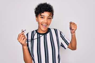 Young beautiful african american afro referee woman wearing striped uniform using whistle screaming...