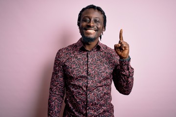 Young handsome african american man wearing casual shirt standing over pink background showing and pointing up with finger number one while smiling confident and happy.