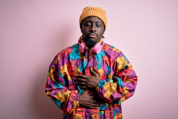 Young handsome african american man wearing colorful coat and cap over pink background with hand on stomach because indigestion, painful illness feeling unwell. Ache concept.