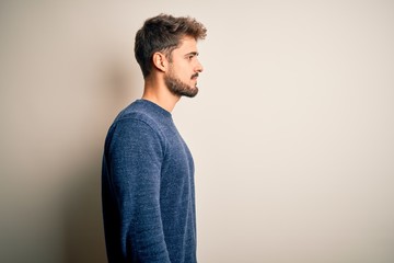 Young handsome man with beard wearing casual sweater standing over white background looking to...