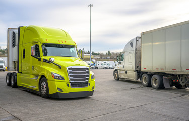 Bright big rig semi truck with refrigerator unit on the semi trailer turning on the truck stop parking lot moving to the exit