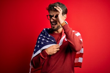 Young man wearing glasses and United States of America flag over isolated red background with happy face smiling doing ok sign with hand on eye looking through fingers