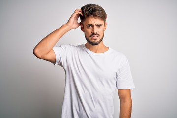 Fototapeta na wymiar Young handsome man with beard wearing casual t-shirt standing over white background confuse and wonder about question. Uncertain with doubt, thinking with hand on head. Pensive concept.