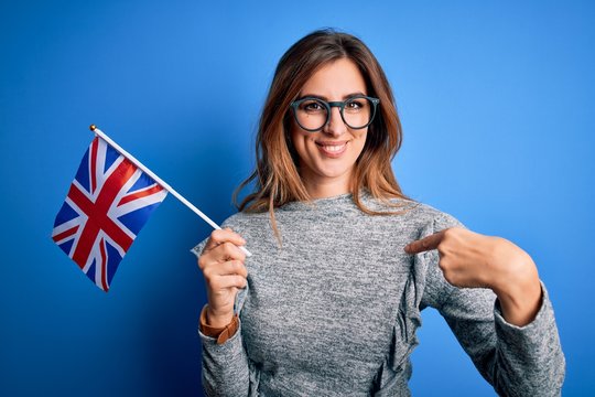 Young beautiful brunette patriotic woman holding united kingdom flag on brexit referendum with surprise face pointing finger to himself - Powered by Adobe
