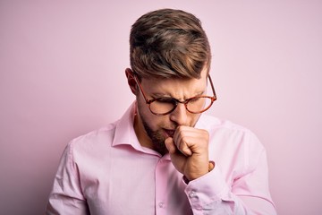 Young handsome blond man with beard and blue eyes wearing pink shirt and glasses feeling unwell and coughing as symptom for cold or bronchitis. Health care concept.