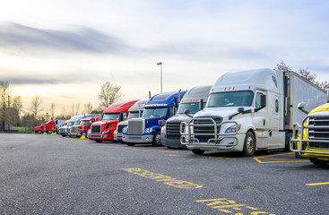 Different big rigs semi trucks with semi trailers standing in row on truck stop parking lot with reserved spots for truck driver rest © vit