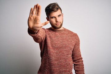 Young blond man with beard and blue eyes wearing casual sweater over white background doing stop...