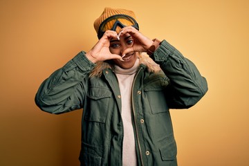Young african american afro skier girl wearing snow sportswear and ski goggles Doing heart shape with hand and fingers smiling looking through sign