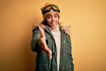 Young african american afro skier girl wearing snow sportswear and ski goggles smiling friendly offering handshake as greeting and welcoming. Successful business.