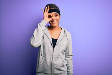 Young african american sportswoman doing sport wearing sportswear over purple background doing ok gesture with hand smiling, eye looking through fingers with happy face.