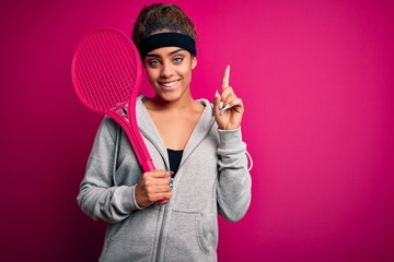 Obraz na płótnie Canvas Young african american sportswoman playing tennis using racket over isolated pink background surprised with an idea or question pointing finger with happy face, number one