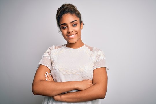 Young beautiful african american girl wearing casual t-shirt standing over white background happy face smiling with crossed arms looking at the camera. Positive person.