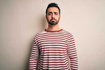 Young handsome man with beard wearing casual striped t-shirt standing over white background depressed and worry for distress, crying angry and afraid. Sad expression.