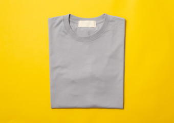 Grey folded t-shirt isolated on yellow background.
